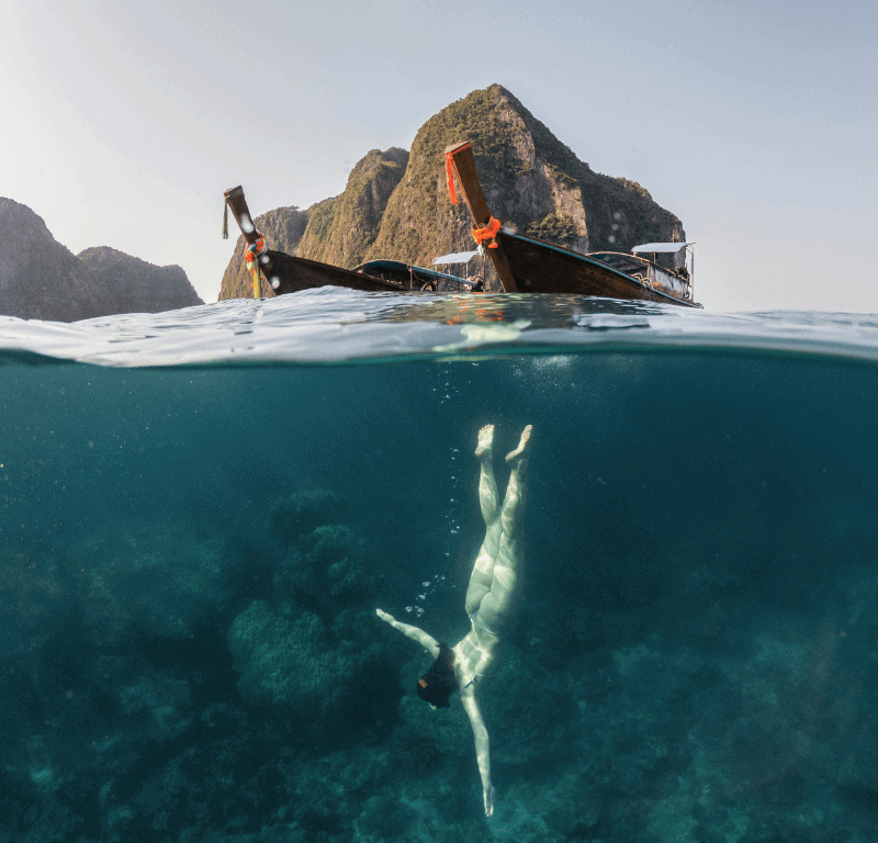 Girl snorkeling with long tail in the background in phi phi island